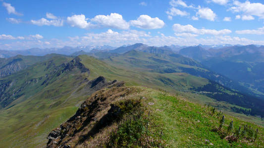 风景秀丽的夏季山景观与绿色的丘陵和山峰和在瑞士阿尔卑斯山微弱的远足小径