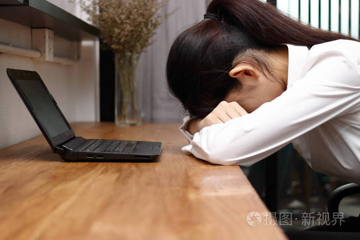 疲惫的劳累过度的年轻的亚洲企业妇女在办公室的办公桌上