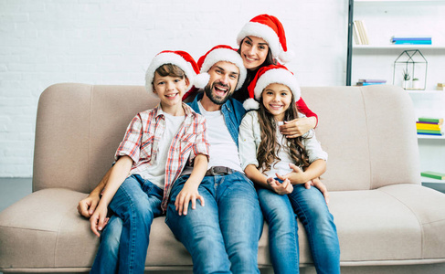 快乐的年轻的家庭在红圣诞老人帽子花时间在客厅里