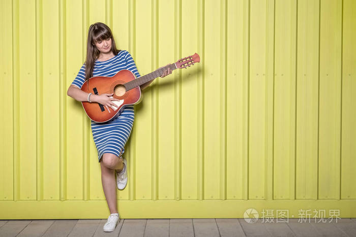 在黄色背景下演奏声学吉他的年轻妇女复制空间