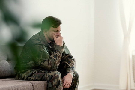 悲伤的士兵穿着制服捂着嘴坐在沙发上