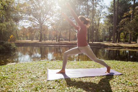 健康的生活方式在大自然中, 妇女做瑜伽运动在垫子在公园附近湖在美丽的早晨秋天天