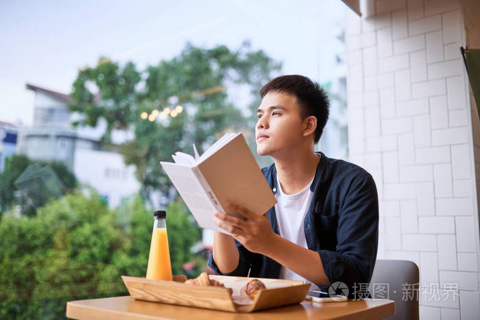 亚洲青年男子看书坐在咖啡馆的餐桌上照片-正版商用图片08uef7-摄图新