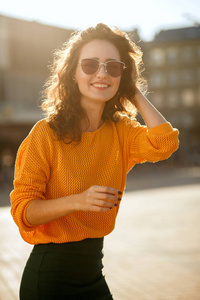 积极的年轻女子戴着太阳镜穿着时髦的衣服, 走在阳光明媚的街道