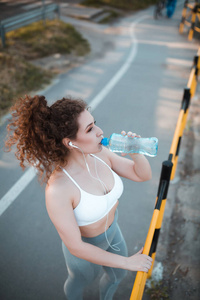 运动中的年轻女运动员在户外运动时饮用瓶装水的画像
