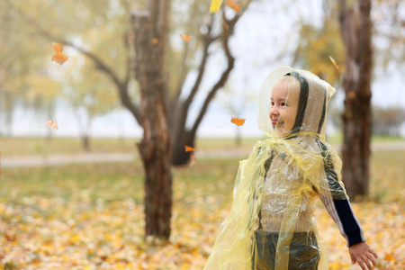 可爱的小男孩雨衣有乐趣在秋天的公园