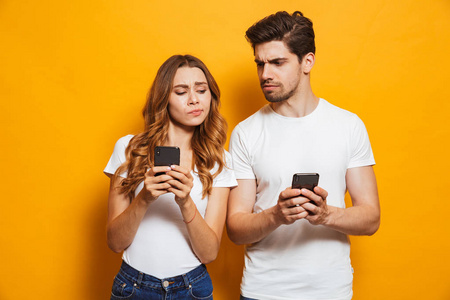 好奇的男人和女人的形象皱眉, 偷看对方的手机, 孤立的黄色背景照片