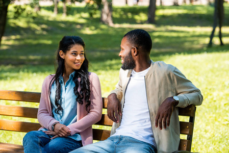 非洲裔美国人夫妇坐在公园的木凳上, 看着对方