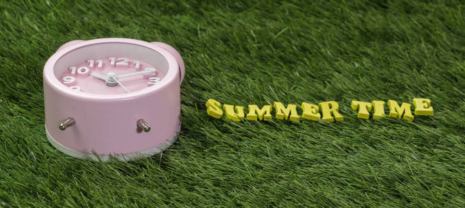 粉红色的闹钟与夏天时间文本在绿色草