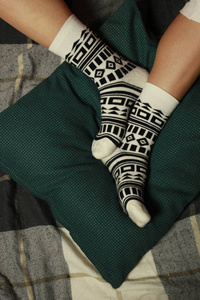 妇女的腿在美丽的袜子与黑色几何正宗装饰品。腿躺在绿色枕头上