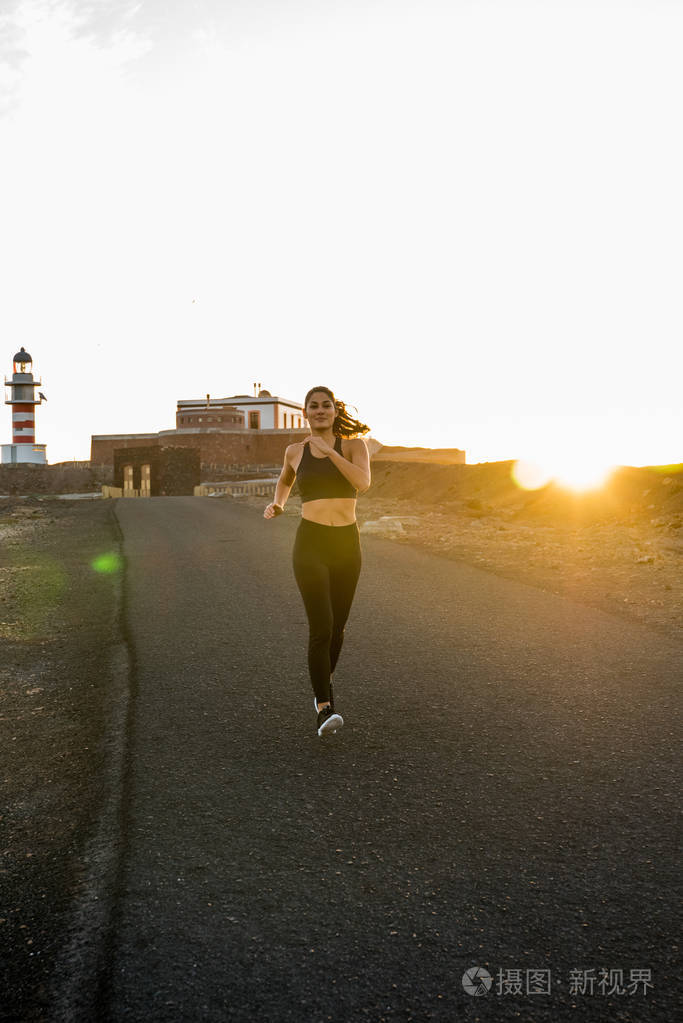 在太阳落山的背景下沿着道路奔跑的女人