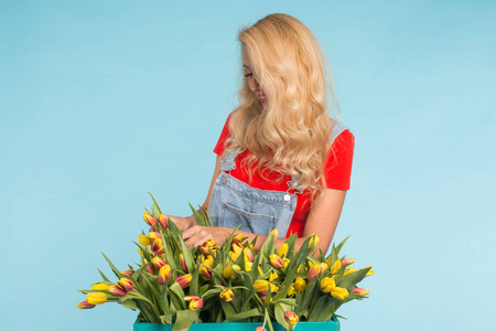 植物区系地理, 假期, 花店和人的概念美丽的金发女郎年轻的妇女固定花束的郁金香在蓝色背景