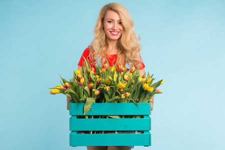 美丽的金发女子园丁藏品盒与郁金香在蓝色背景