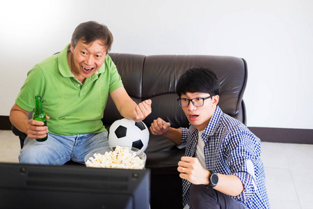 亚洲足球支持者小组的朋友看足球比赛在电视上和欢呼, 庆祝与啤酒和爆米花在家中与乐趣或失望图释