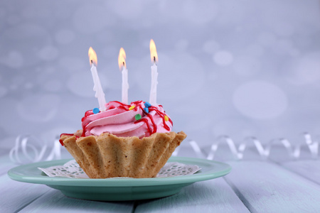 色木桌和浅色背景板上的蜡烛的生日杯蛋糕