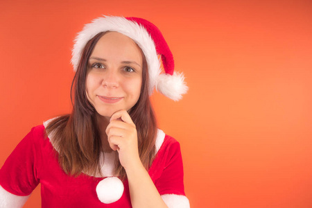 在橙色背景打扮成圣诞老人的年轻女孩的肖像。新年快乐, 圣诞快乐