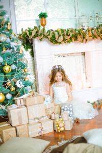 可爱的小女孩与长卷曲的头发在家里附近的圣诞树与礼品和花环和装饰的壁炉