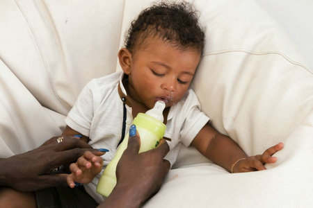 可爱的婴儿看起来可疑地在瓶牛奶。母亲用牛奶喂养婴儿孩子