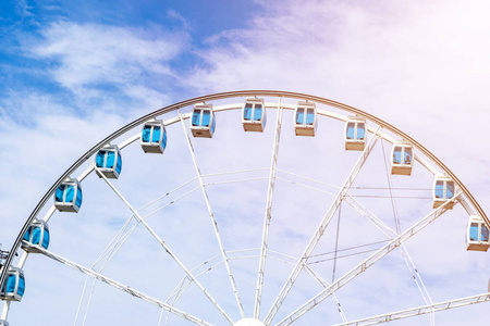 在一个蓝色的天空背景的游乐园的摩天轮的低角度视图。城市公园摩天轮在传送带花园。度假理念