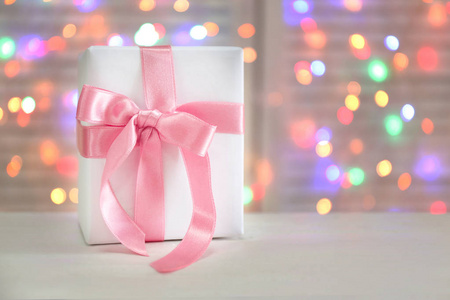 在桌子上的礼品盒与粉红色的丝带对脱焦的灯