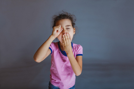 女孩在他的眼睛在灰色背景打呵欠 t 手照片