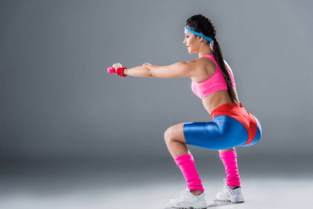 女孩的侧视图运动的女孩做蹲在灰色的哑铃侧视图照片