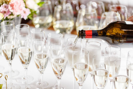酒保将香槟或葡萄酒倒入餐厅餐桌上的酒杯中。隆重举行的婚礼或新年快乐晚宴