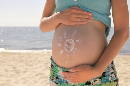 防晒霜上一个女人怀孕的肚子，在沙滩上的