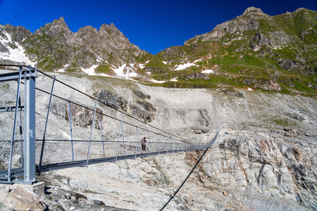 在瓦莱州瑞士阿尔卑斯山附近的一条山路上, 徒步行走在 Corbassiere 冰川上的吊桥上的女性徒步旅行者