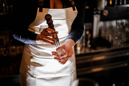 女酒保粉碎一块冰, 使一个新鲜的夏季鸡尾酒在酒吧柜台
