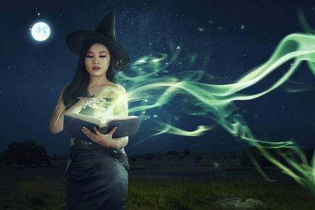 亚洲女巫的女人美丽的亚洲女巫从书本上学习魔术法术的夜晚照片