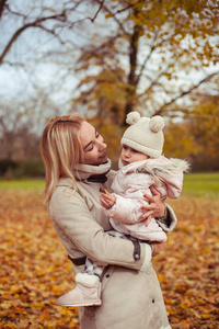 年轻的母亲和小女儿在秋天散步。妈妈和女儿玩。温暖的冬天明亮的秋天。舒适