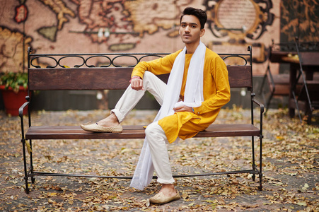 印度时尚男子在黄色的传统衣服白色围巾摆在长凳上户外