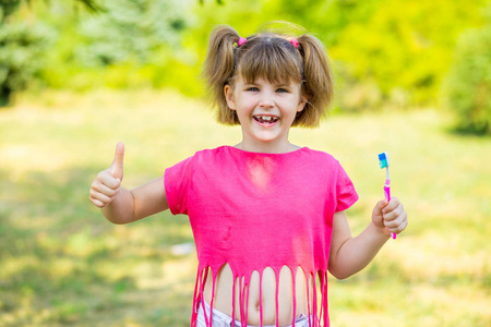 快乐的小女孩用大拇指刷她的牙齿。牙科卫生。健康理念