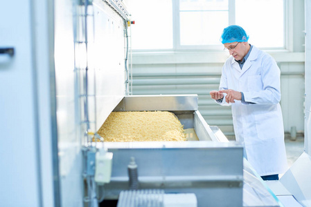 高级工厂工人肖像在食品厂的质量检查站在机器单位与通心粉, 复制空间