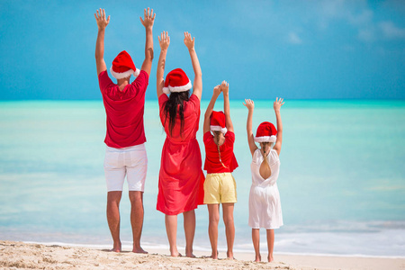 在一个热带海滩上庆祝圣诞假期的红色圣诞老人帽子的幸福家庭