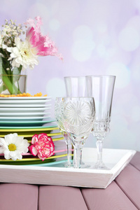 堆多彩陶瓷餐具和鲜花的托盘，木桌前，在明亮的背景上