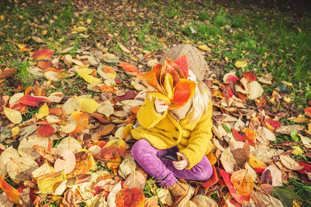 美丽的女孩，微笑着的金发女郎玩秋天的树叶