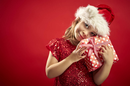 可爱的小女孩在圣诞礼服在圣诞老人的帽子与圣诞礼物