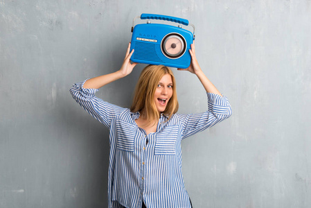 金发女孩拿着一个蓝色的复古收音机纹理难看的垃圾墙背景