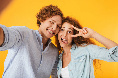 内容的图像夫妇男人和女人拿着自拍的照片, 而显示和平标志与微笑孤立的黄色背景