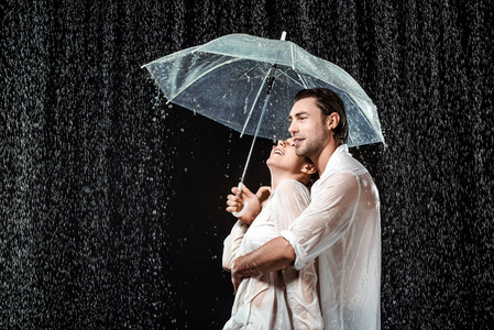 在黑色的雨滴下站在雨伞下的浪漫情侣的侧面视图照片