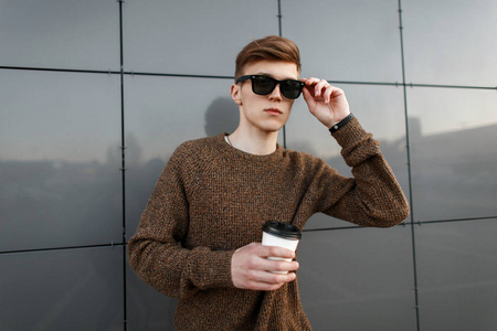 英俊时髦的人与咖啡校正太阳镜在街道附近墙壁