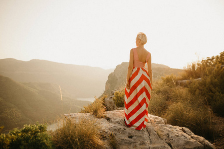 一个穿着红色衣服的年轻女子, 在橙色的日落中, 她的背在古老的峡谷里摆姿势。西班牙