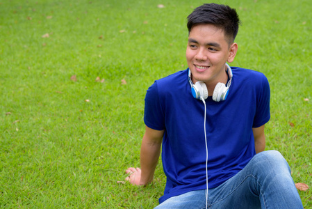 年轻英俊的亚洲男人带着耳机在公园里放松