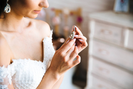 在婚纱礼服上的一个年轻女孩的裁剪框架特写检查耳环。新娘的指甲, 婚礼的装饰品。新娘费的概念, 上午