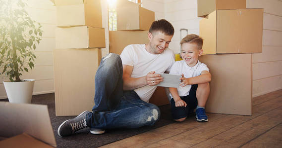 家人在搬家的时候在新房子里装纸板箱。父亲和孩子在新的房子。父子坐用数码片