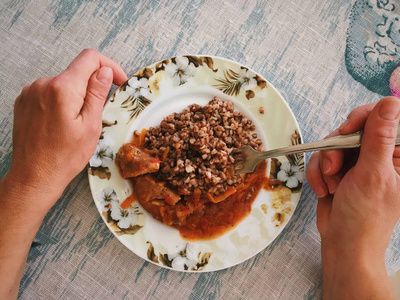 手在盘子里拿叉子, 用荞麦和煮肉在蔬菜酱