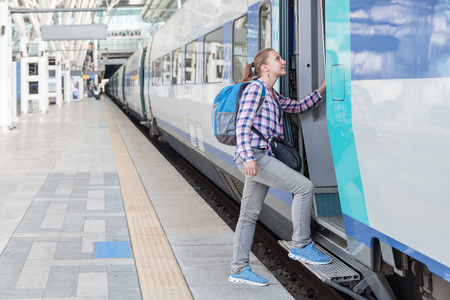 年轻的女游客进入火车。在火车站带着蓝色背包的漂亮女人。铁路旅行。现代高速列车