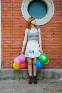 有彩色气球的年轻妇女在砖墙背景上
